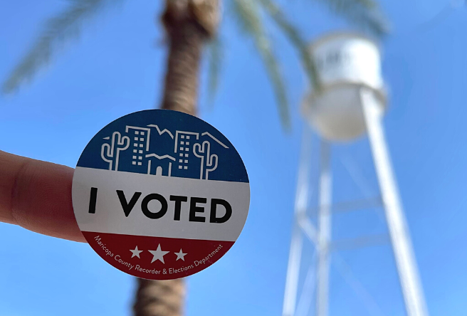 An 'I Voted' sticker is being held up in front of the Gilbert Water Tower.