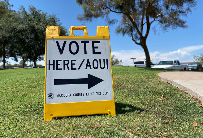 A yellow 'Vote Here/Aqui' sign outside a Gilbert Vote Center.