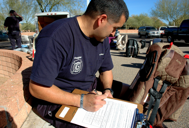 A male firefighter taking notes while looking at a car seat.