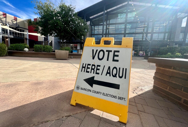 A photo of a yellow 'Vote Here/Aqui' sign at a Gilbert Voting Center.