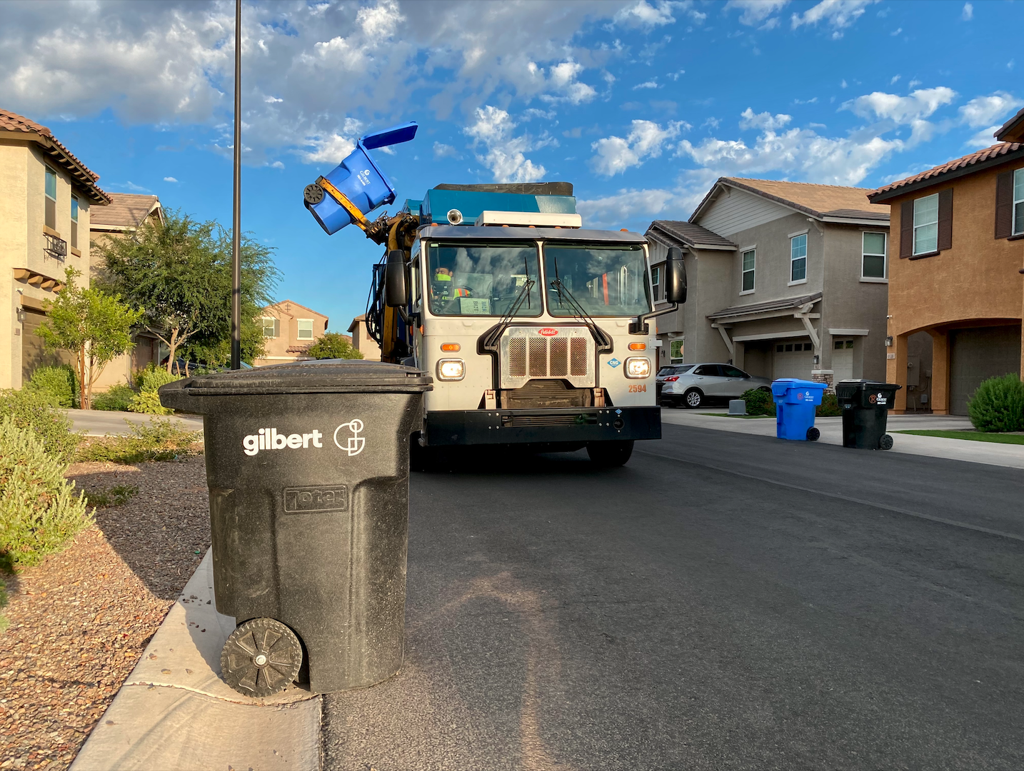 A Gilbert garbage truck services a blue recycling can a it makes its way through town.