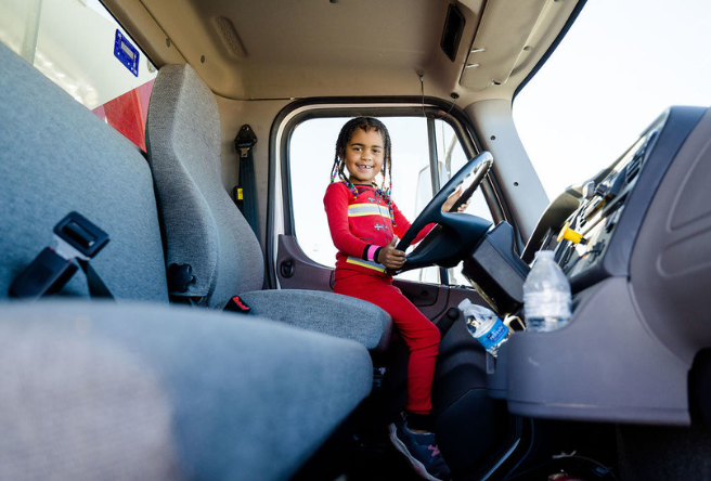 A young child climbs in the driver's side of a very large truck at Truck-A-Palooza 2022.