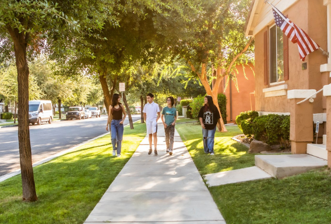 A group of kids walking through a Gilbert neighborhood with green grass and trees.