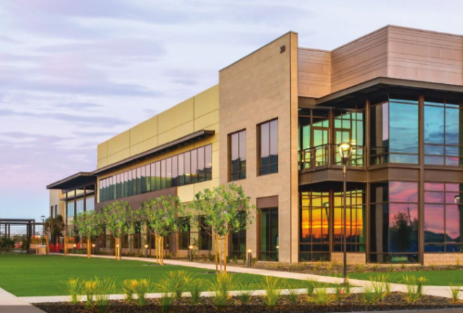 Photo of an office building with green space in the front and a sunset in the background.