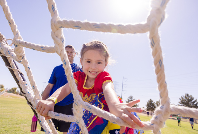 A young girl climbing a net wearing a Wonder Woman outfit.