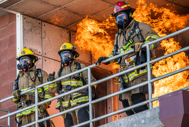 A group of Gilbert Firefighters stand against a railing as a fire rages behind them during a training exercise in Gilbert.