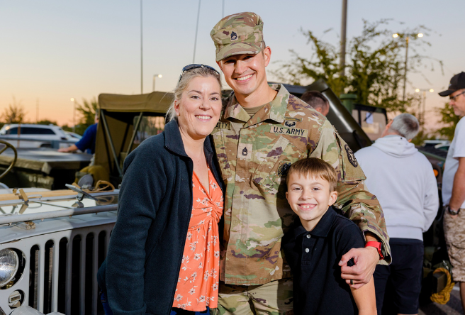 A male army veteran poses for a group photo hugging his wife and son.