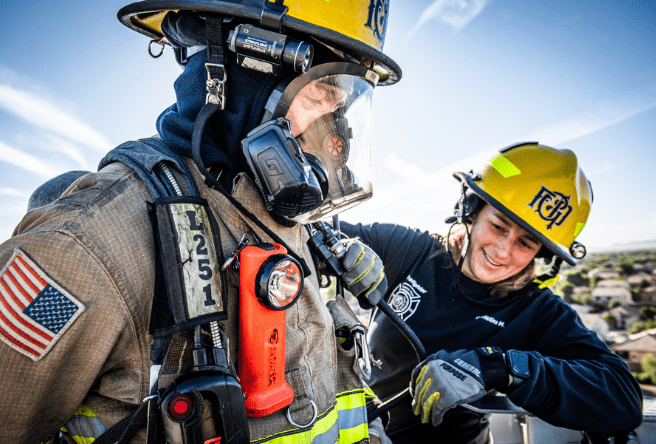 Two firefighters, one in full uniform, stand side-by-side.