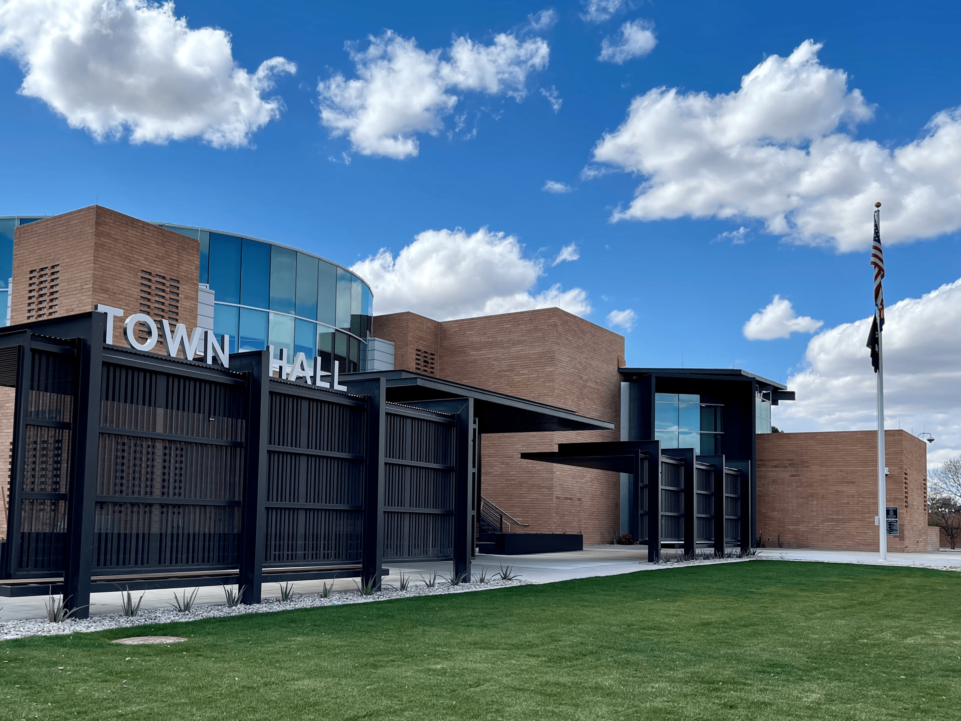 A wide shot of the outside of town hall showing the entrance, American flag, and blue cloudy skies.