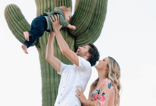 A man and woman play with their young child next to a cactus at the Riparian.