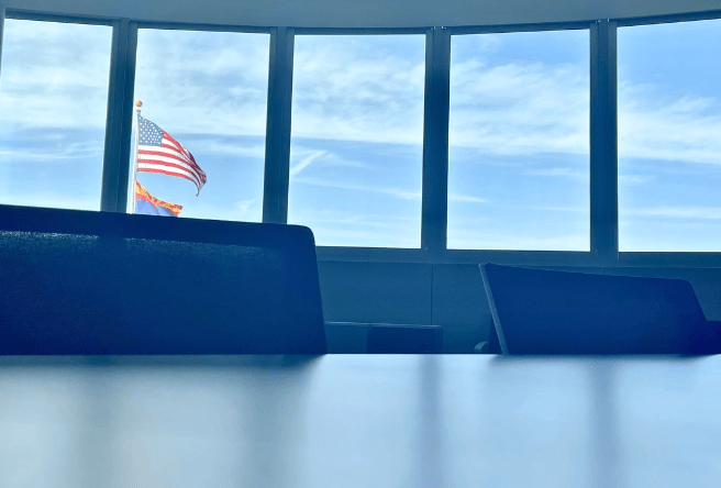 A wideshot from inside the Heritage Room at Town Hall showing two chairs at a table and the American and Arizona flags outside.