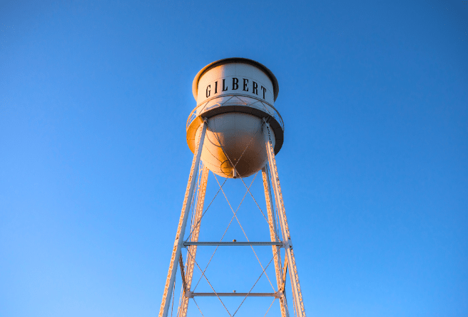 A wideshot from the ground showing the Gilbert Water Tower in the sky as the sun rises from the east.