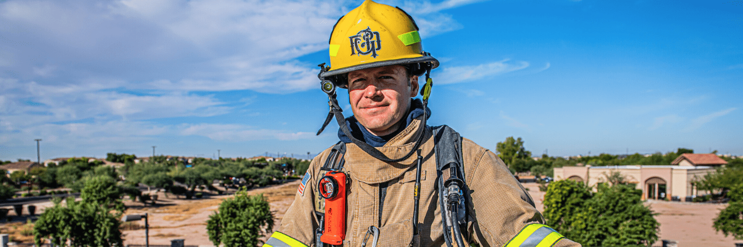 A male firefighter poses in full uniform with the skyline behind him.