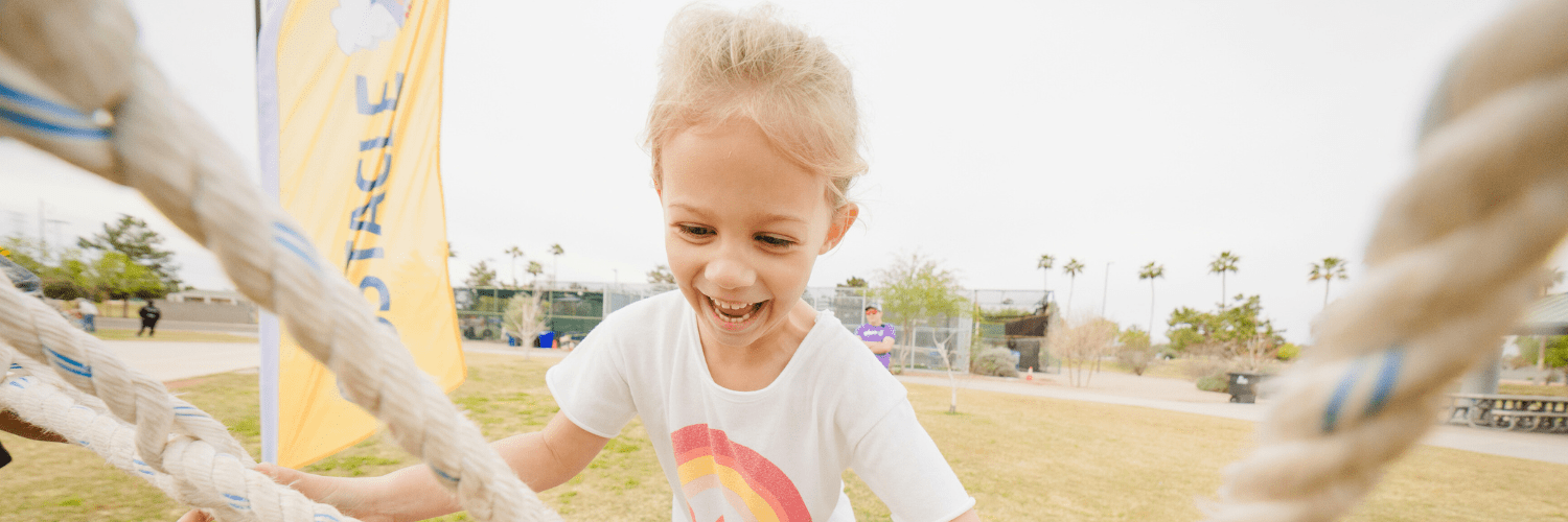 A young girl is photographed while climbing up a large rope obstacle course.